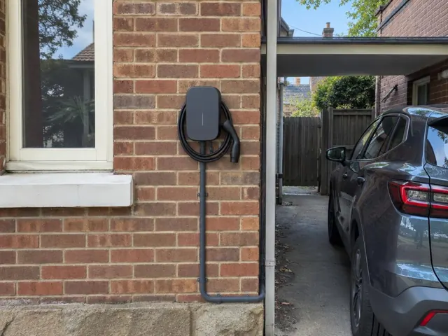 Wall-mounted EV charger on a brick exterior wall beside a window and driveway in North Sydney