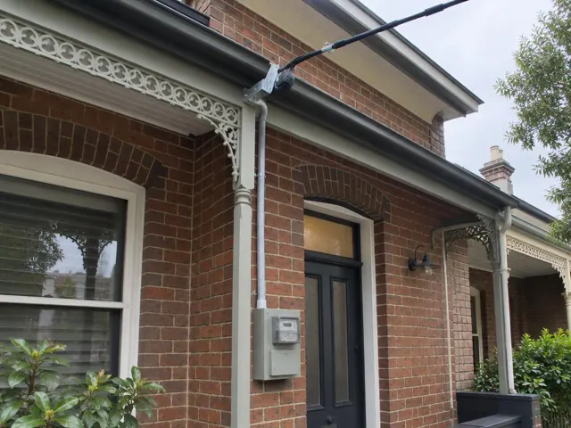 Brick house facade with overhead service cable and point-of-attachment bracket on the eaves in Neutral Bay